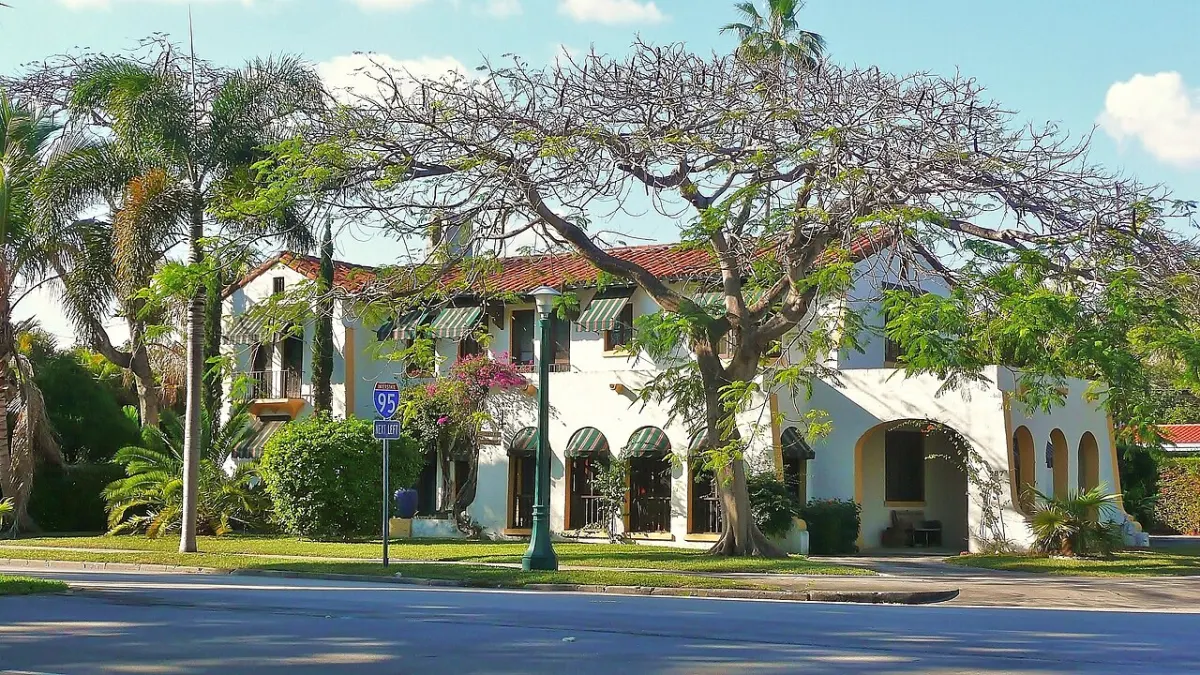 A two-story Mediterranean-revival house behind mature trees in Miami Shores
